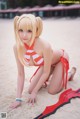 A woman in a red and white bikini crouching on the beach.