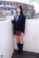 A woman in a school uniform leaning against a wall.