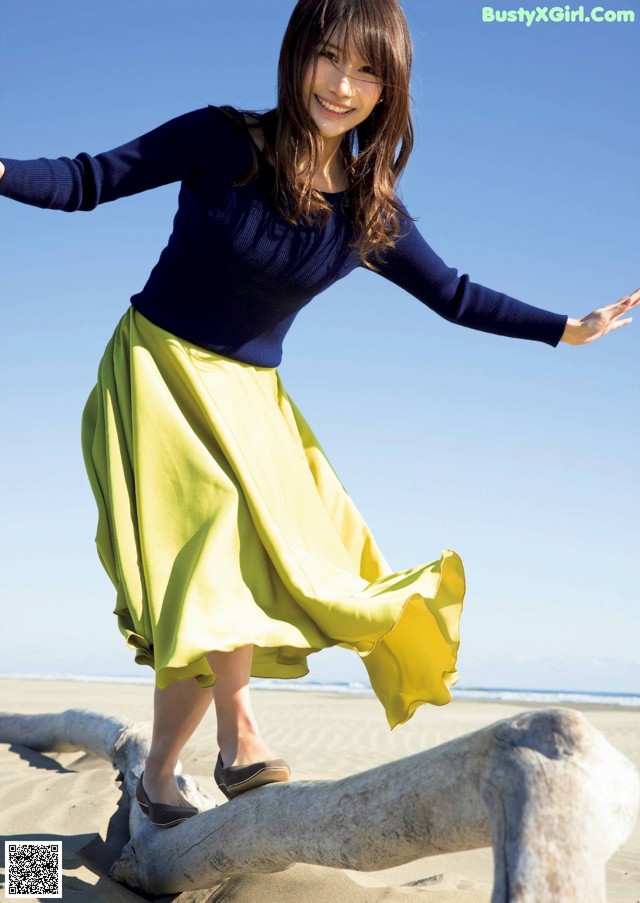 A woman standing on top of a log on the beach.