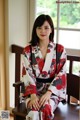 A woman in a red and black kimono sitting on a chair.