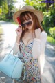 A woman in a dress and hat holding a blue bag.