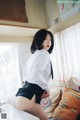 A woman in a white shirt and black skirt sitting on a bed.
